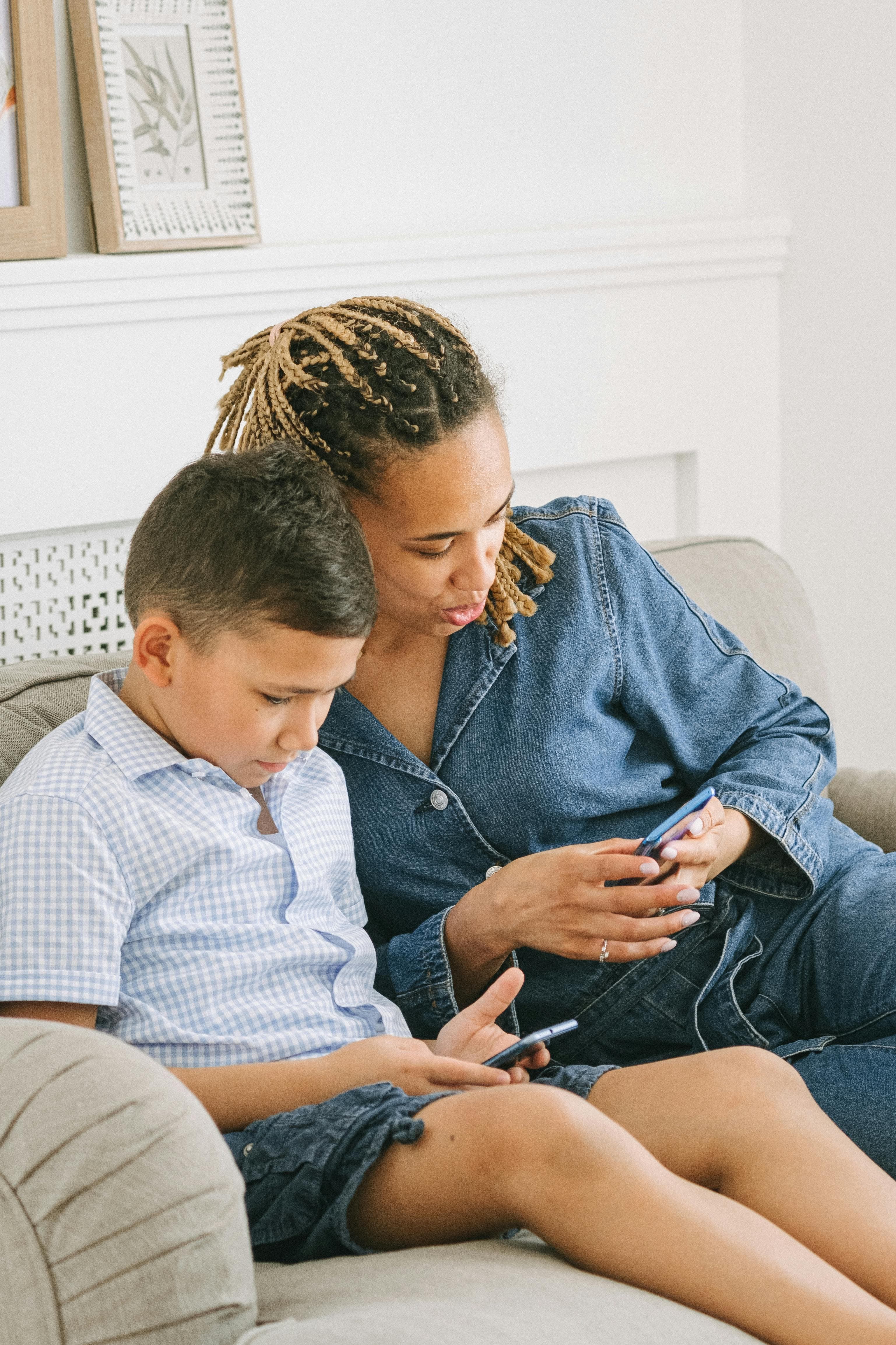 A parent and child looking at a phone together on the sofa